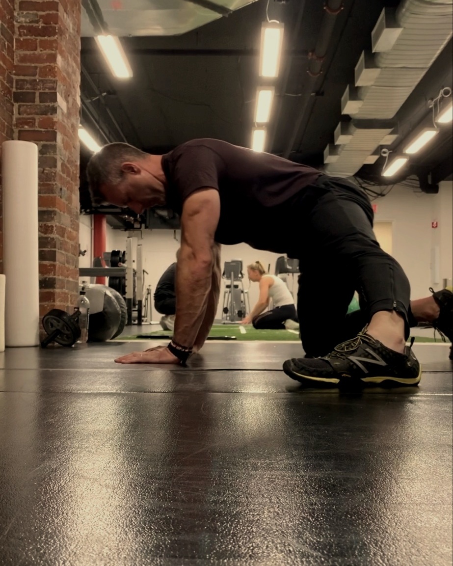 Brandon Kolar in a low push-up plank position, coaching in the gym